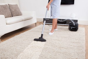 Cropped image of young maid cleaning carpet with vacuum cleaner at home